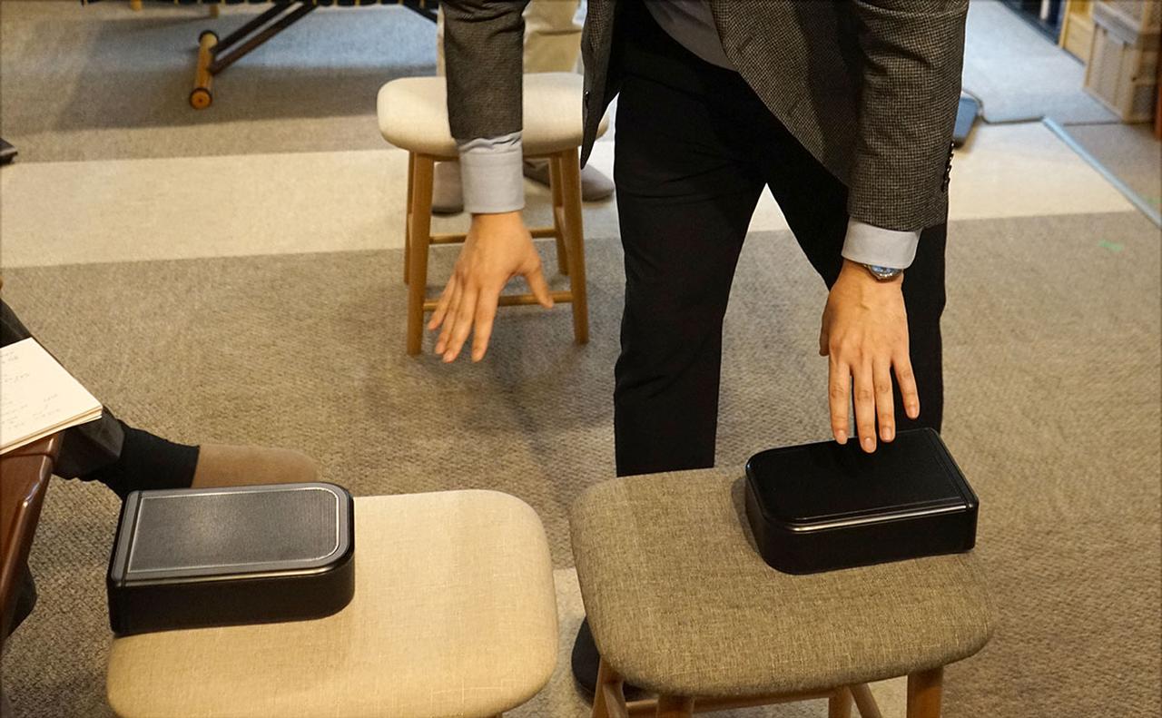 画像: 取り外したワイヤレスリアスピーカーを試聴位置（写真のふたつ並べた椅子の中央）の両脇に置いて、サウンドバーから視聴者までの距離を測定する