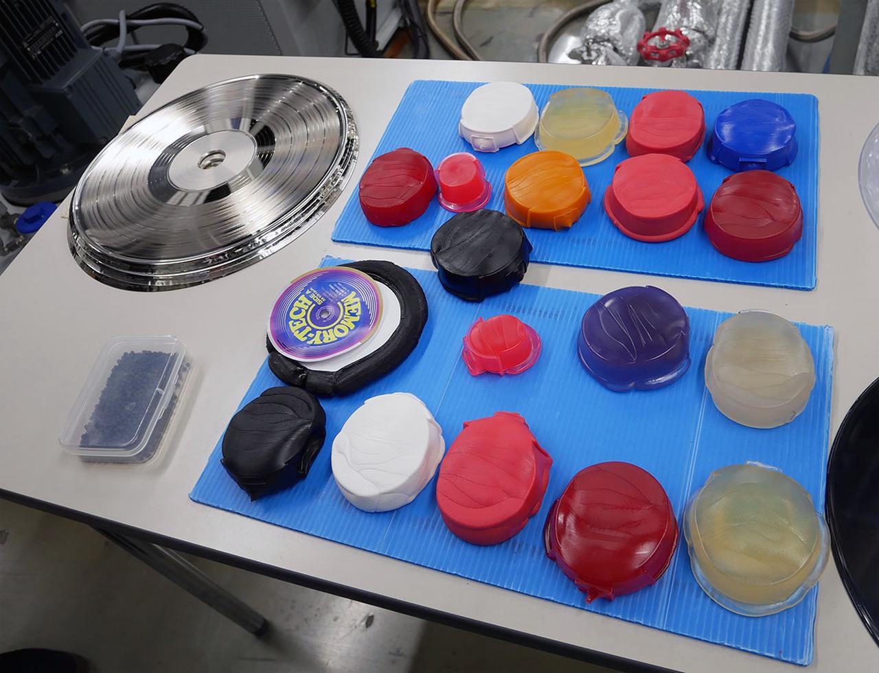 画像: アナログレコードは、スタジオでカットしたラッカー盤を元にメタルマザー/スタンパーを作り、そのスタンパーを塩化ビニールに押し付けて成型することで作られている。写真左の銀盤がスタンパーで、右は様々な種類の塩化ビニール