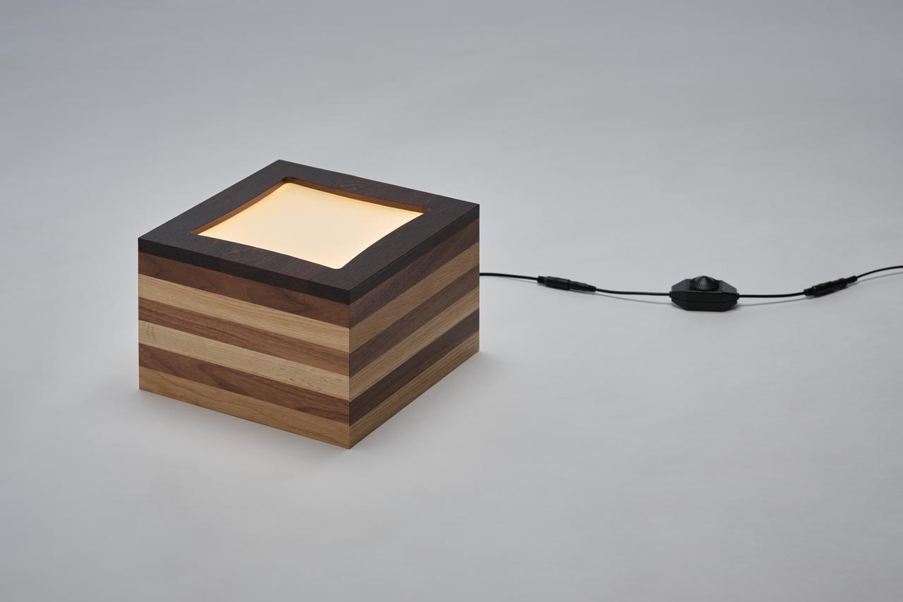 画像: 「Light Gift」3種類の木材を使用し、素材そのものの色差でボーダー模様を表現した照明。スクエア状の直線的なデザインの中で、緩やかな曲線のディテールがアクセントとして機能する。卓上照明のほか、吊り照明としても使用できる