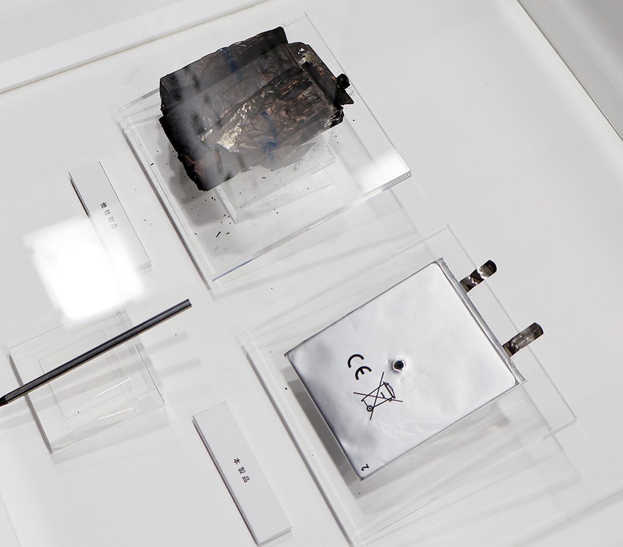 画像: モバイルバッテリーへの釘挿しテスト。右は新仕様の新製品。挿しても発火しません、の展示