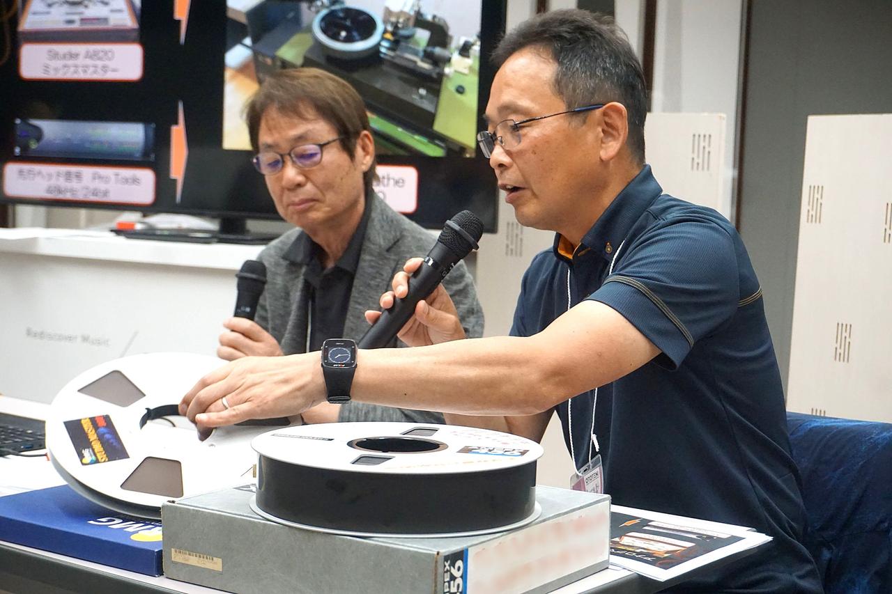 画像: 高田氏(左)とキング関口台スタジオの高橋氏(右)。テーブルに置かれているのは16chアナログマルチ録音で使用されたものと同様の2インチ・アナログテープ。高橋氏が左手に持つのは、ミックスダウンに使われたものと同様のハーフインチアナログテープ