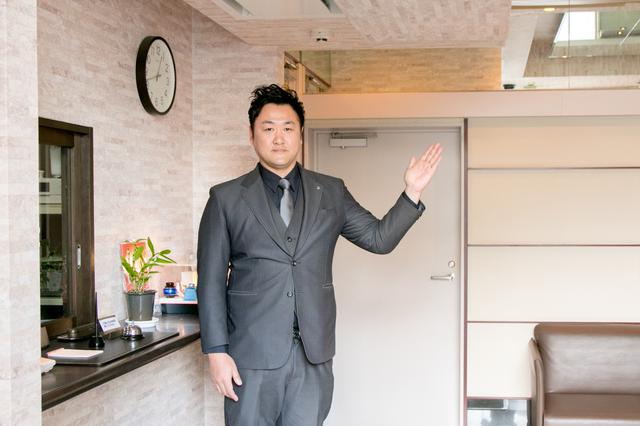 画像: 道路に面した入り口を入ると、左側に受付窓口。右側にはエレベーターがある。 スタッフの後ろに見えるドアは、駐車場に続いている