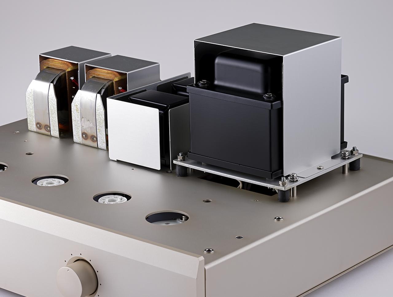 画像: トランスカバーを外した状態。左の出力トランスはスウェーデン・ルンダール製を採用。中央に2基のチョークコイルを配置し、左右ch独立の電源回路を構成する。右端が電源トランスで、モノーラルパワーアンプMA5000から採用された防振ゴムを用いるフローティング構造を採用。この免振構造により、電源トランスの振動がシャーシを経由し、他のパーツに与える影響を可能な限り抑えている。また、珪素鋼板素材のシールド板を各トランスとチョークコイルの周囲に取り付けることで、漏洩磁束の制御が図られている。