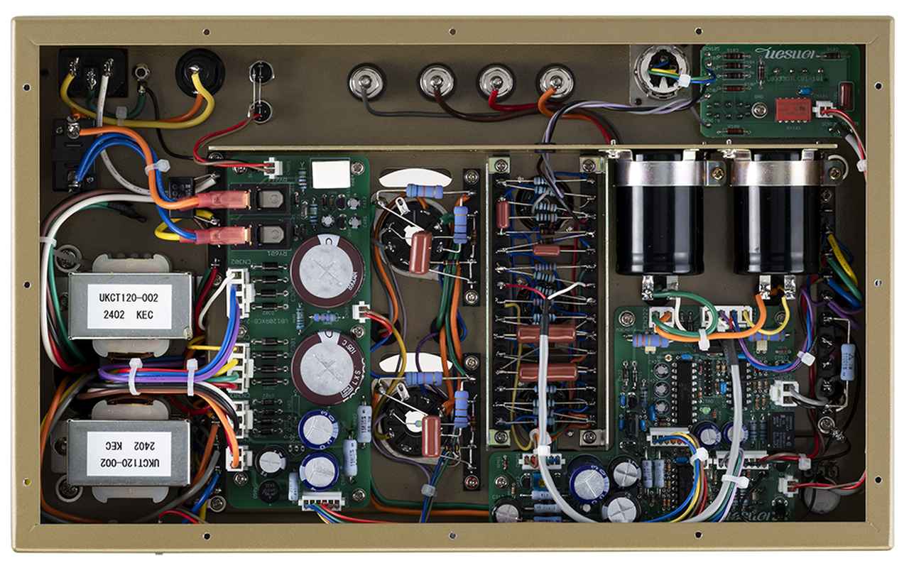 画像: 底板を外すと手配線と基板を効率的に融合した内部が現われる。写真の左側に2つ並んでいるのは出力段電源回路用チョークトランスで、その右側には整流回路を展開。出力管のソケットまわりの右側は順に、バランスの負帰還回路、バイアス調整／保護回路基板（前方）と2基の出力段用メインコンデンサー（後方）などが配置されている。