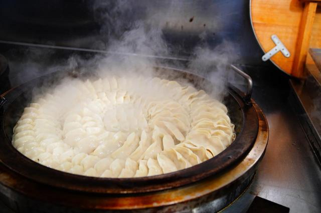 画像: 直径1m以上の鉄鍋で一気に100個の餃子を蒸し焼きに。その様子は壮観