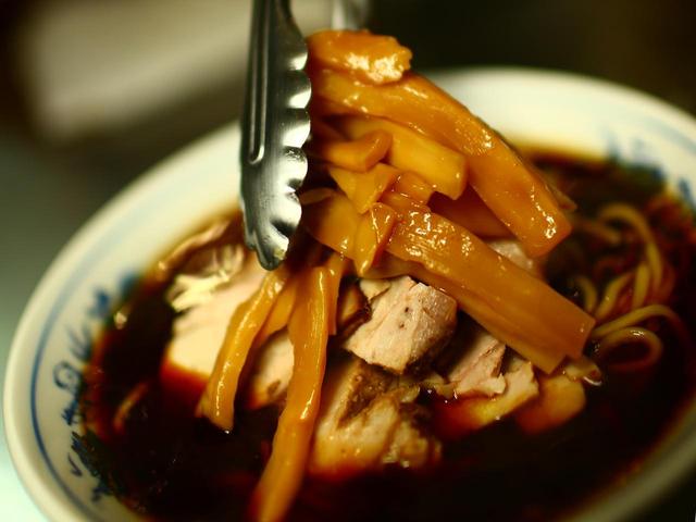 画像: 富山ブラックは最後にメンマを乗せて完成する。このメンマも塩漬けされていて麺と絡むと絶妙な味わいと歯ごたえに変化する