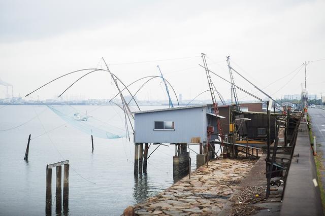 画像: 防潮堤から張り出した海上の小屋と、伸びる四つ手網。電灯で魚をおびき寄せる夜には、また独特の景観が生まれる