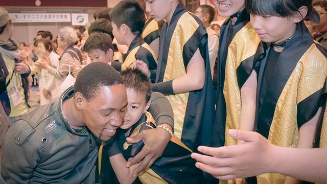 画像: 会場を後にする選手たちと、笑顔と拍手で送り出す住民たち