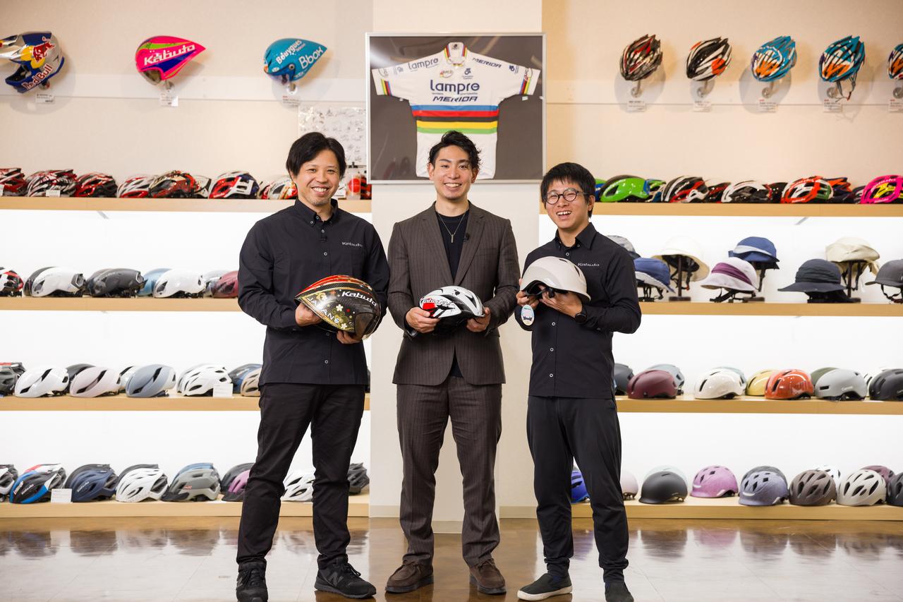 画像: さまざまなタイプのヘルメットが飾られたショールームで感想を語る小原選手