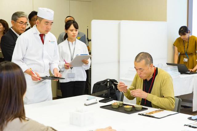 画像: 試食する石川さんを緊張した面持ちで見つめる、JRCのファーストクラス調理担当・西浦嘉明シェフ