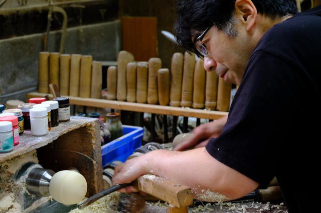 画像: 平賀雅幸さんの作業の様子。足でろくろの回転を操作しながら手元の工具で削りだしていきます。