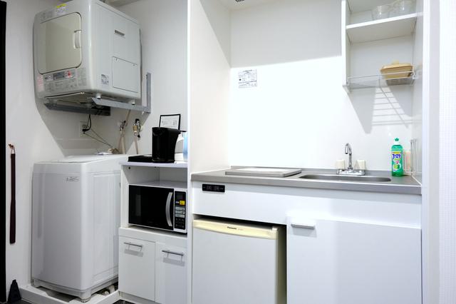 画像: 部屋入口には冷蔵庫、洗濯機などの家電、コンロがあるキッチン。お皿やグラスも揃っています。