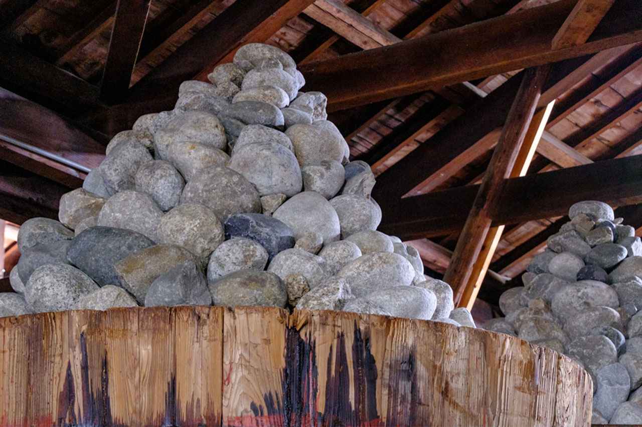Image: River stones are piled up in a cone shape on top of the wooden barrels to act as weights, allowing the miso to mature slowly.