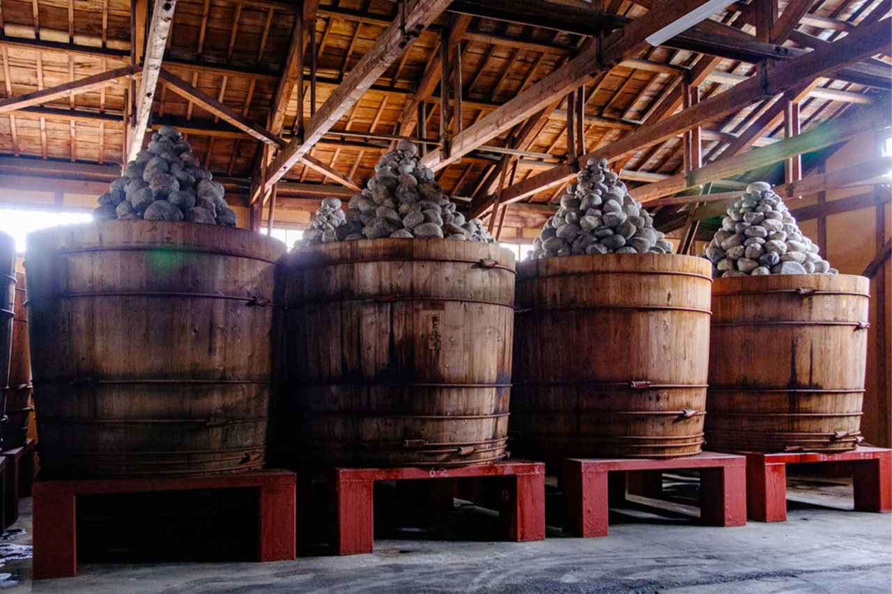 Photo: Inside the solemn storehouse, rows of wooden barrels are lined up where miso is aged slowly and quietly, for at least two summers and two winters (for a minimum of two years).