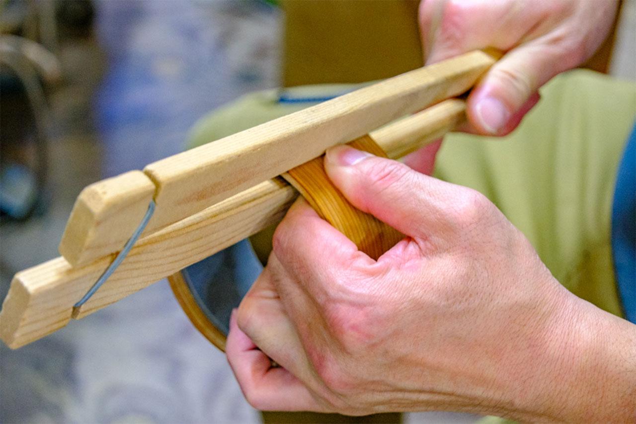 画像: 薄くスライスした秋田杉を型に巻き付け、木バサミ（継ぎ目を留め置く道具）で留めていく