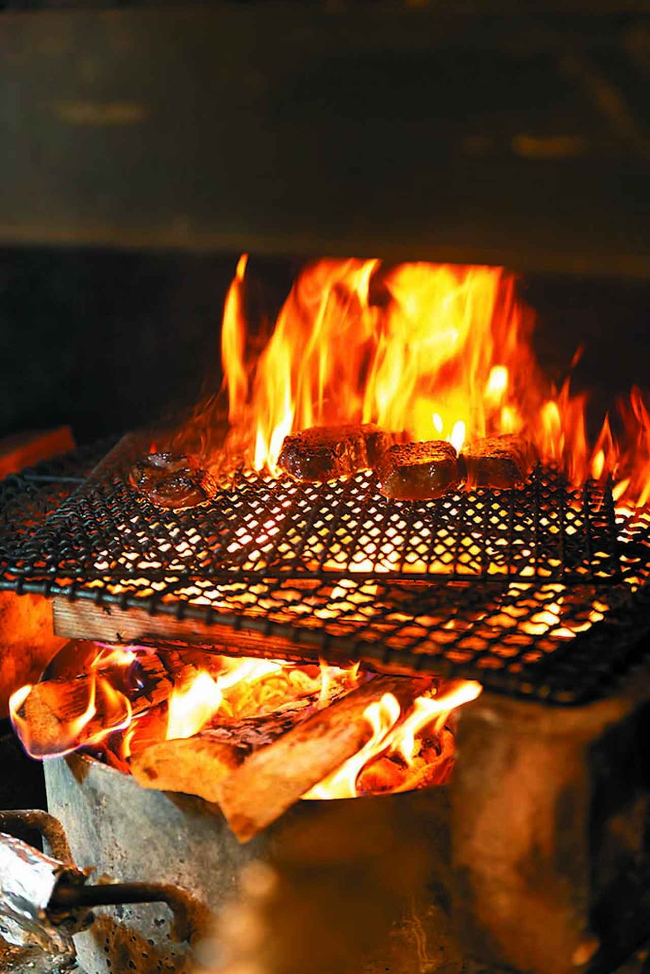 画像: オープンキッチン内に設えた薪釜で大塚シェフが牛、豚、鹿、仔羊を焼く。炭火と違い、高温の直火で焼く薪釜焼きは一気に火が入り、燻香も豊か