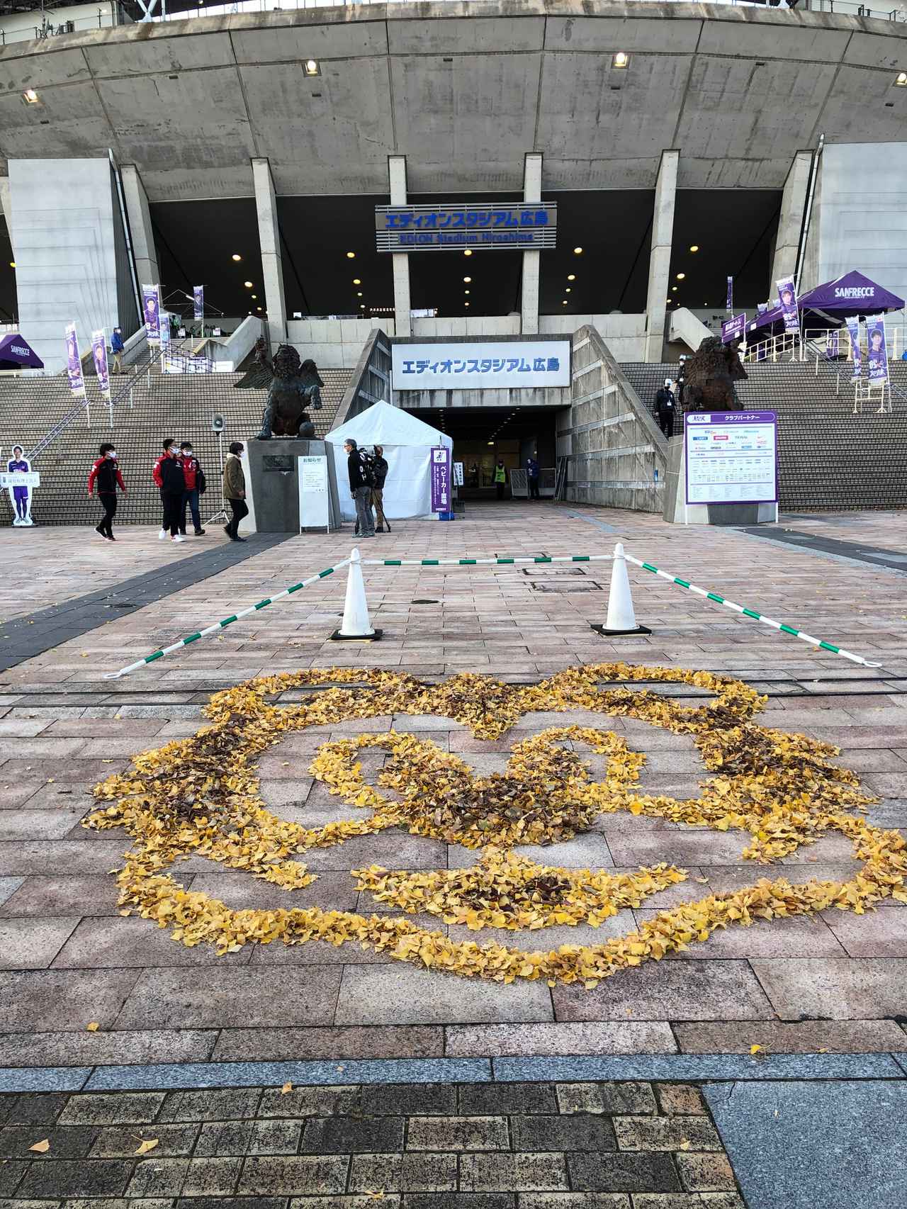 画像 : 2番目の画像 - エディオンスタジアム広島の周辺では、いちょうの鮮やかな黄色が。落ち葉を片付けていたスタッフが、サンチェの顔を作って来場者をもてなした（写真◎石倉利英） - サッカーマガジンWEB