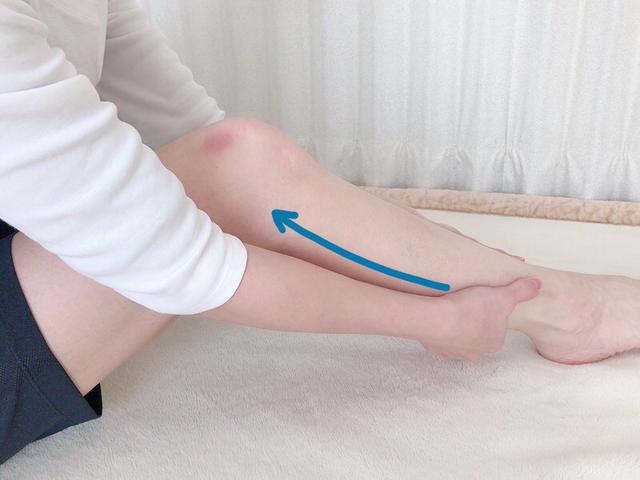 画像: 足首を両手でつつむように持ちます。手をその状態にしたまま、ひざまで滑らせます。この動きを10回ほど繰り返します。