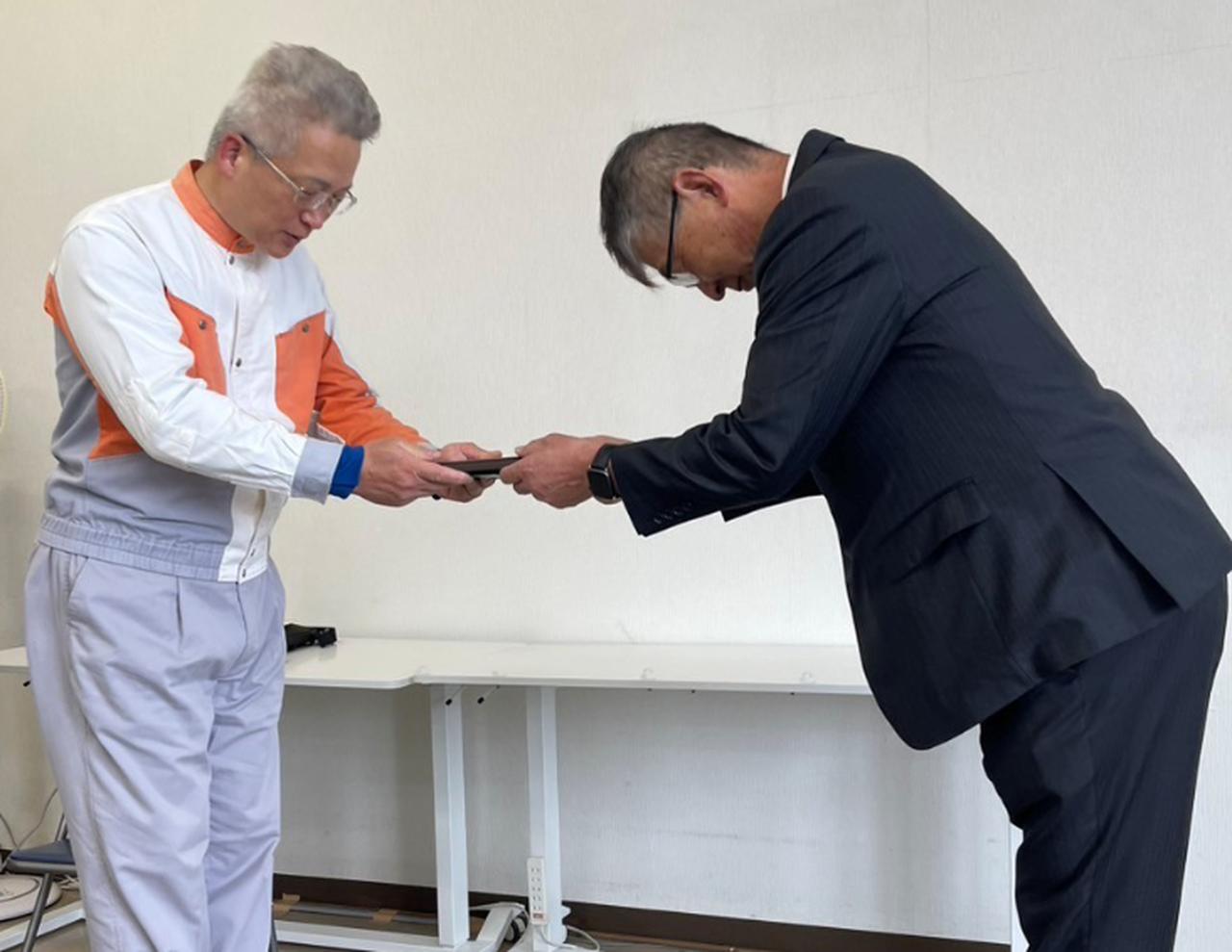 画像: 滋賀での表彰伝達式。県安協の横江一郎課長（写真右）から表彰盾を手渡される森特指