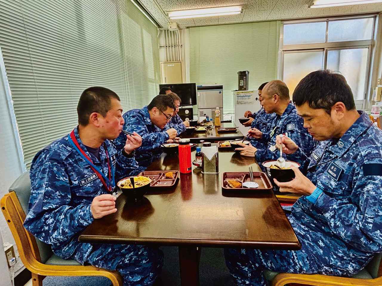 画像: 長いテーブルに隊員が向かい合って食事をする。距離が近く、まるで家庭の食卓のような雰囲気だ