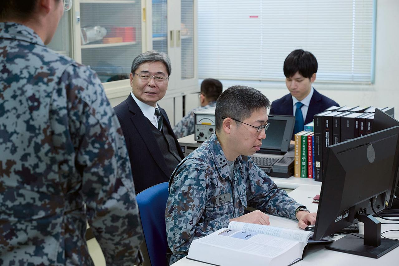 画像: 研究部署には自衛官だけでなく防衛技官（※写真奥背広を着た2人）も配置されている。松井1尉は「彼らとの連携も部署の運営上、とても重要だ」という
