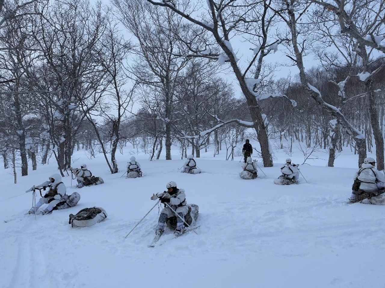画像: 行動停止中は、雪面からの冷気で体を冷やさないよう、あえてザックの上に座ることもある