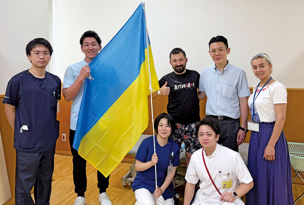 画像: 2024年7月、自衛隊中央病院が受け入れたウクライナ負傷兵の元へ、一時帰国の際に激励に訪れた笛田1佐（後列右から2番目）。負傷兵、病院スタッフらと撮影
