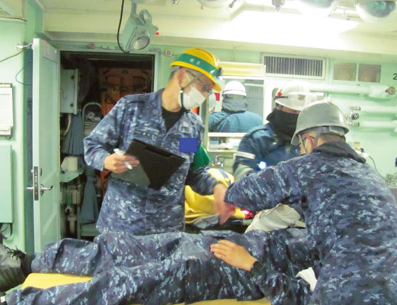 画像: 負傷者が発生した際の応急処置などを行う衛生の訓練。チェック項目を確認し、1秒を争う治療活動の適切な処理法などを助言する指導官(左)