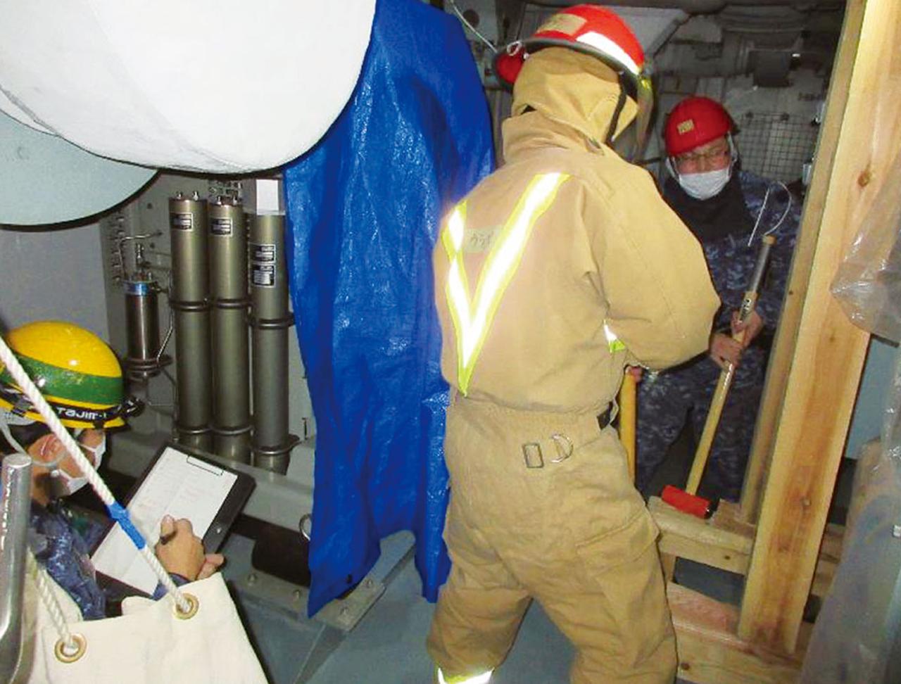 画像: 艦艇が攻撃を受け、船底に穴が開いた際の応急工作の訓練。指導官(左下)は適切な対応ができるかの評価と合わせ、作業時間も計測する