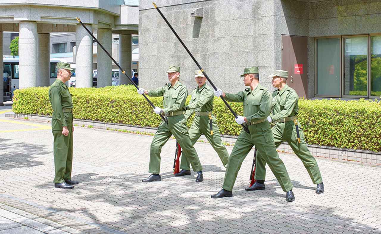 画像: 儀じょう隊で国旗を掲げる旗手は、何があっても旗を手放してはならないという重責を担う。そこで、強風にあおられても旗が飛ばされないように、旗衛隊員が旗手を後方で支えて安定させる訓練も行われる