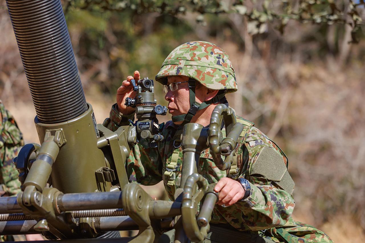 画像: 照準具をのぞいて、精密に方角を測定する分隊員。わずかな角度のずれで砲撃は当たらない