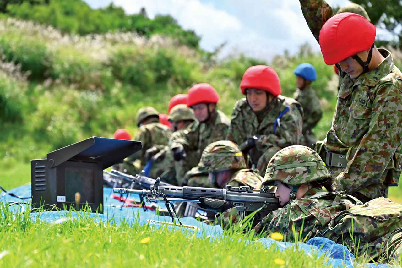 画像: 予備自の射撃訓練。訓練中は、赤いヘルメットをかぶり射手に対して指導する射撃係が付く。青いヘルメットをかぶった、射撃中の安全管理を担当する安全係が現場の安全を確保する