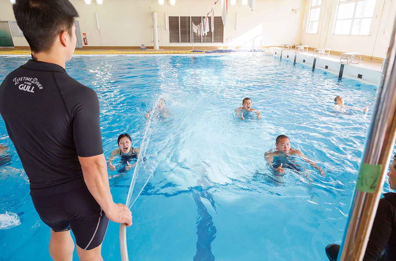 画像: 立ち泳ぎ中、教官がホースで水を掛ける。救難員の活動現場は悪天候であることを想定した訓練