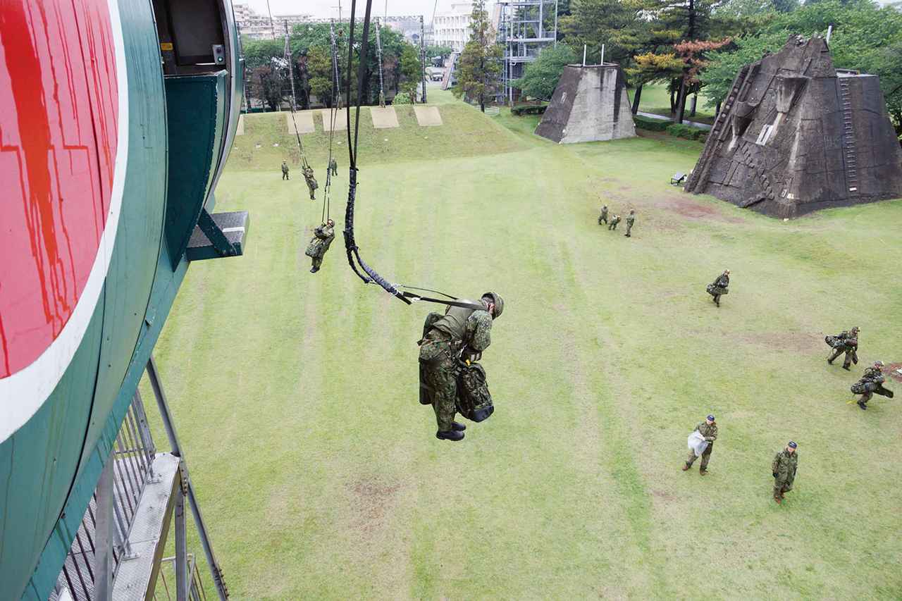 画像: フル装備で跳び出した学生要員は、跳出塔から約60メートル先の土手まで、張られたワイヤにぶら下がり滑降。跳び出して4秒後に上を見て、傘が開いているかを確認する動作を学ぶ