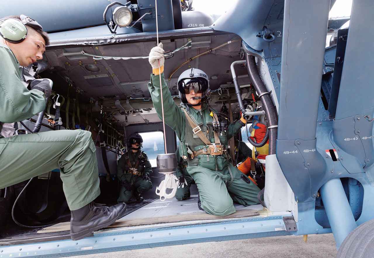 画像: 機上整備員課程のホイスト訓練は最初は地上で実機を使って行う。エンジン音で会話はできないため、身振りで指示を出す