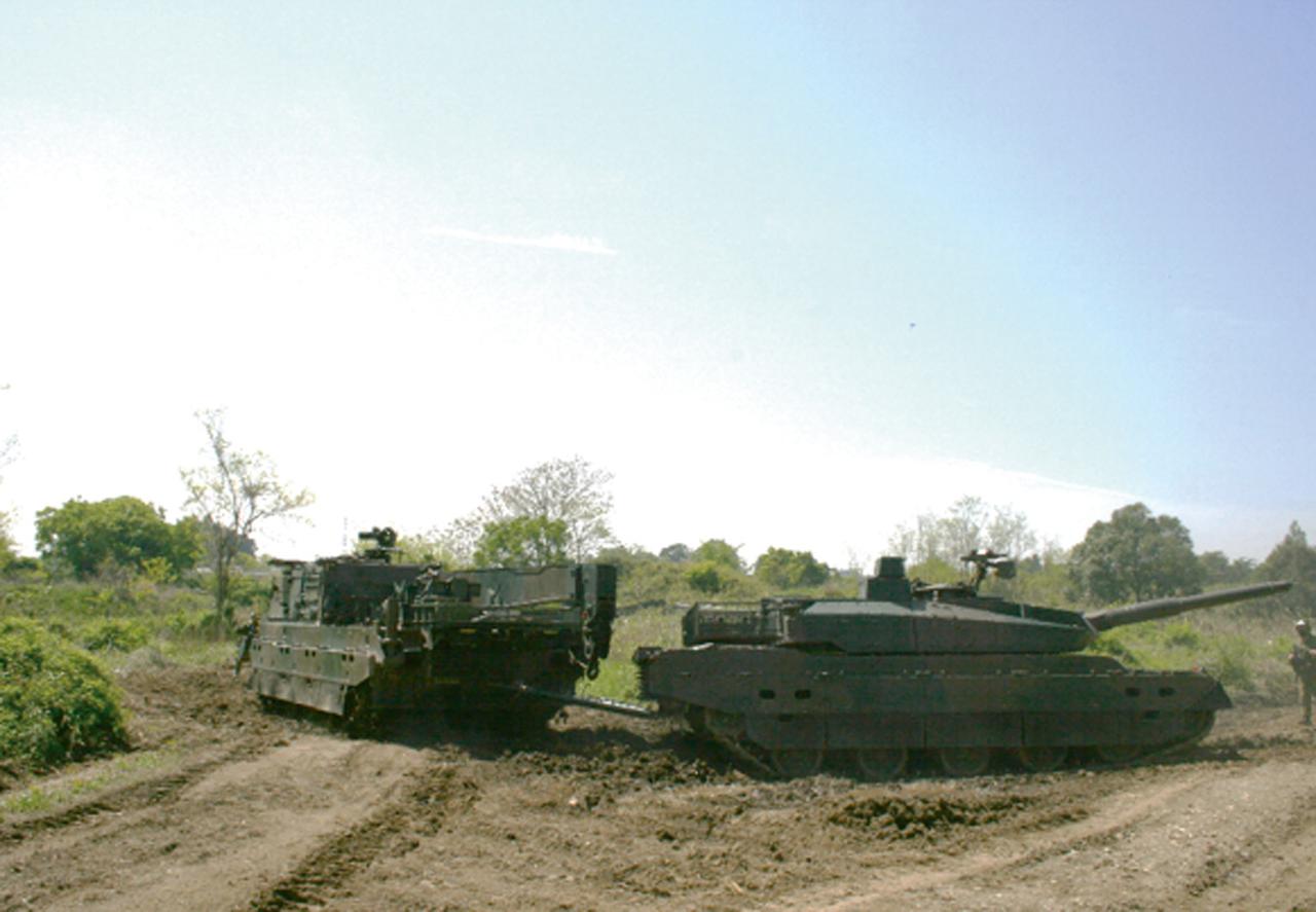 画像: 10式戦車（右）をけん引する11式装軌車回収車。トーバを走行不能になった戦車に付け敵のいない地域まで運ぶ