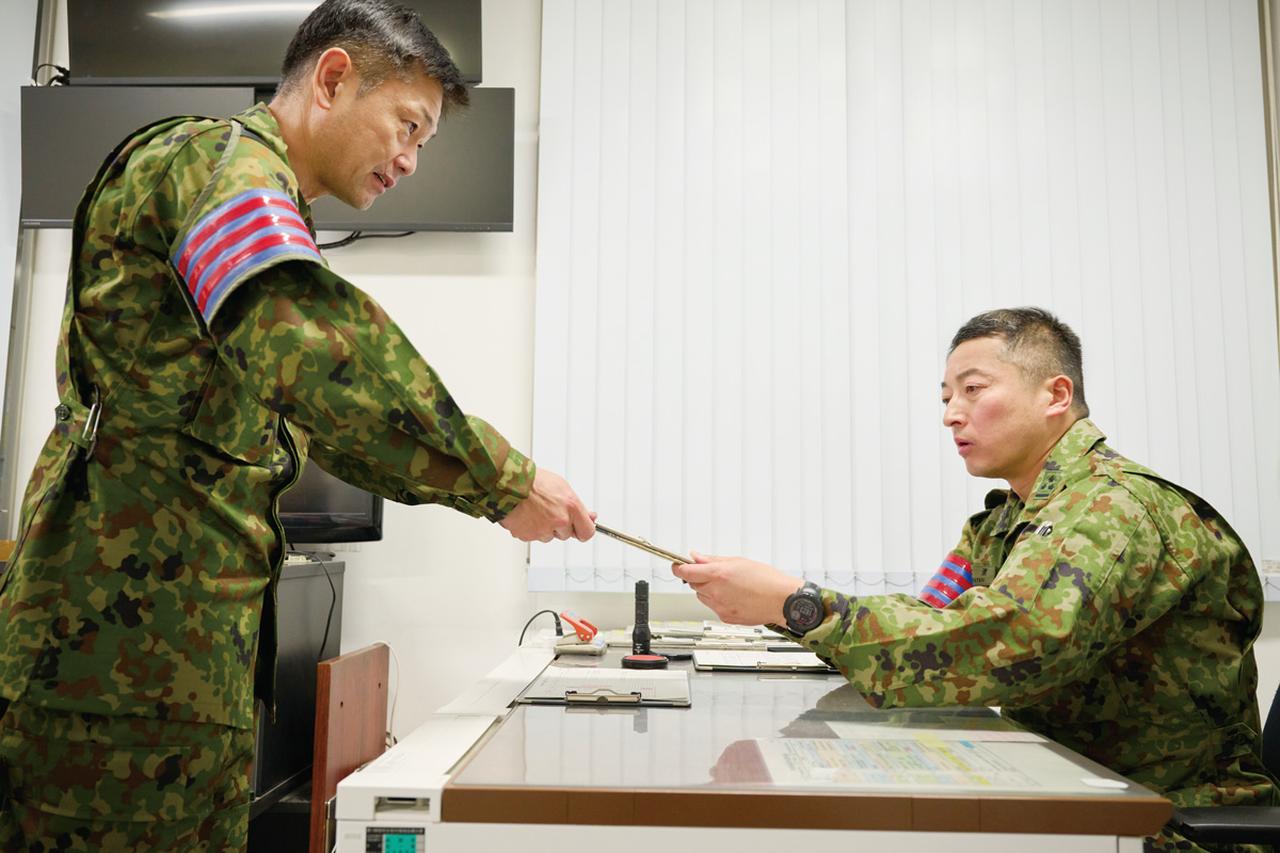 画像: 駐屯地当直司令（右）の承認を得るため、書類を提出する駐屯地当直副官。駐屯地に出入りする業者の予定や人数など、当直勤務中は駐屯地の警備に関するさまざまな事務作業を行う