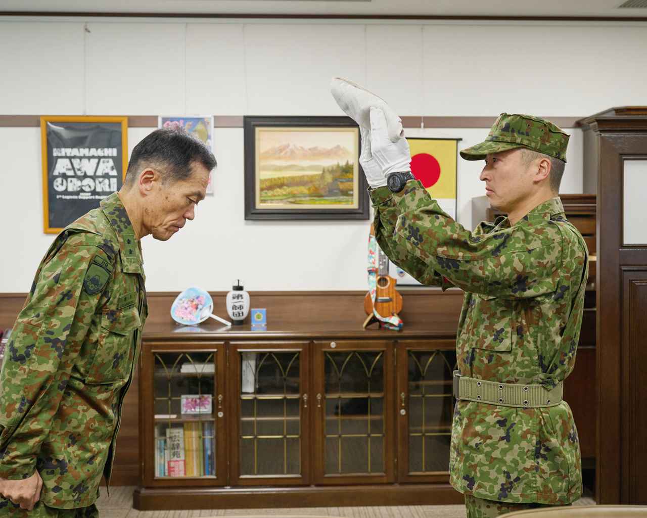 画像: 駐屯地司令室に収められている国旗を持ち出す駐屯地当直司令（右）。駐屯地司令は国旗に敬礼し、国旗掲揚が行われる