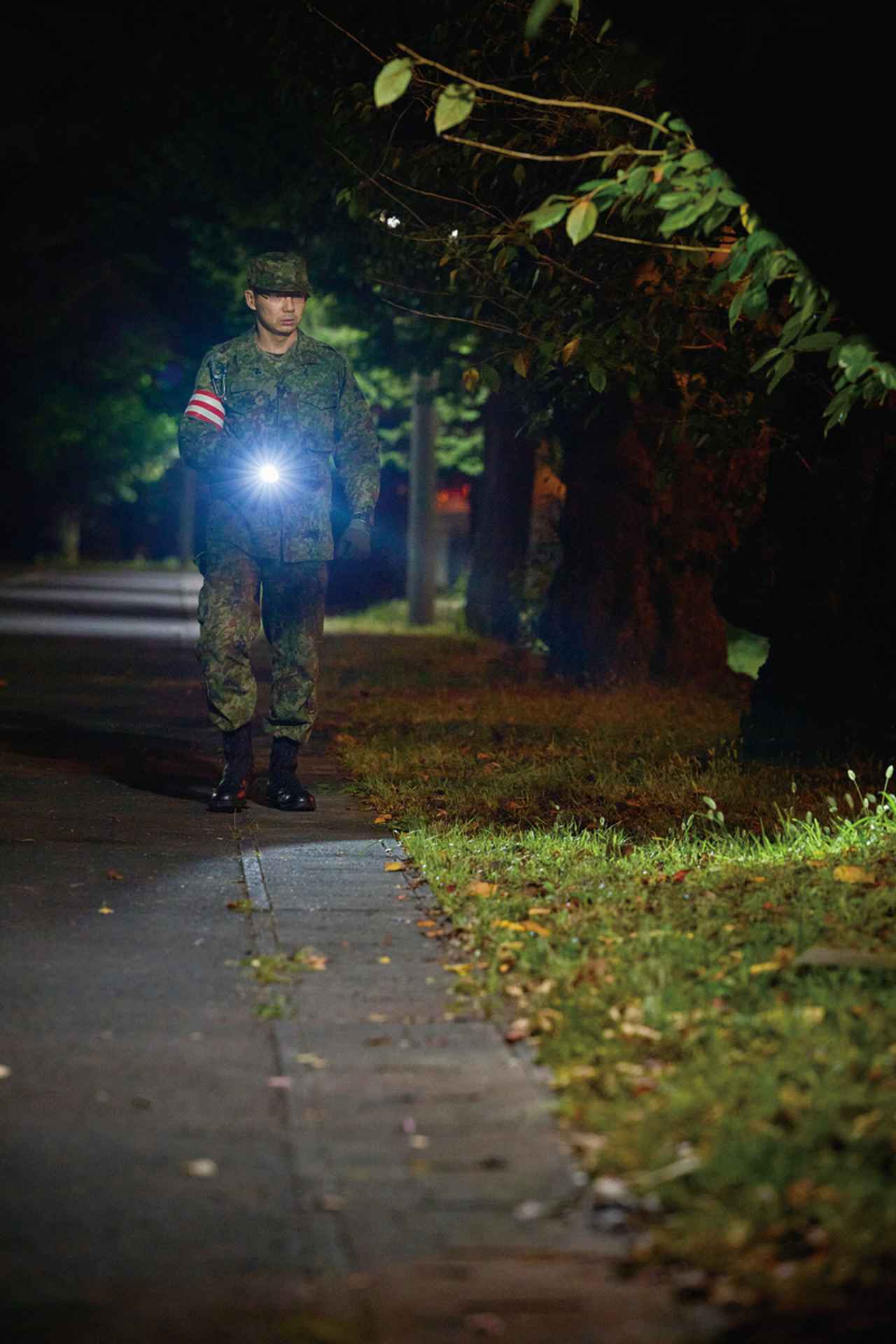 画像: 駐屯地内を巡察する当直勤務者。物陰や車両の下など見落としやすい場所まで丁寧に確認していく