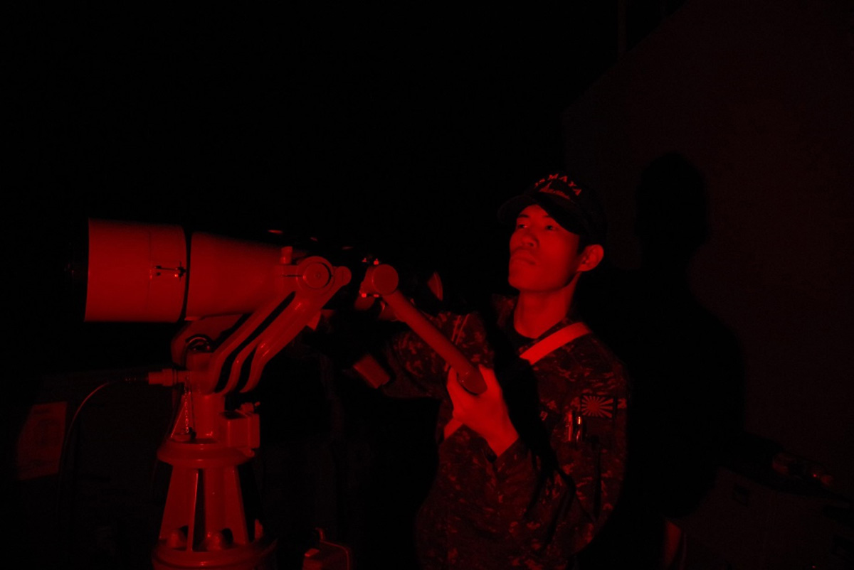 画像: 夜間、赤色灯のもとで双眼鏡を使い周囲を警戒する隊員