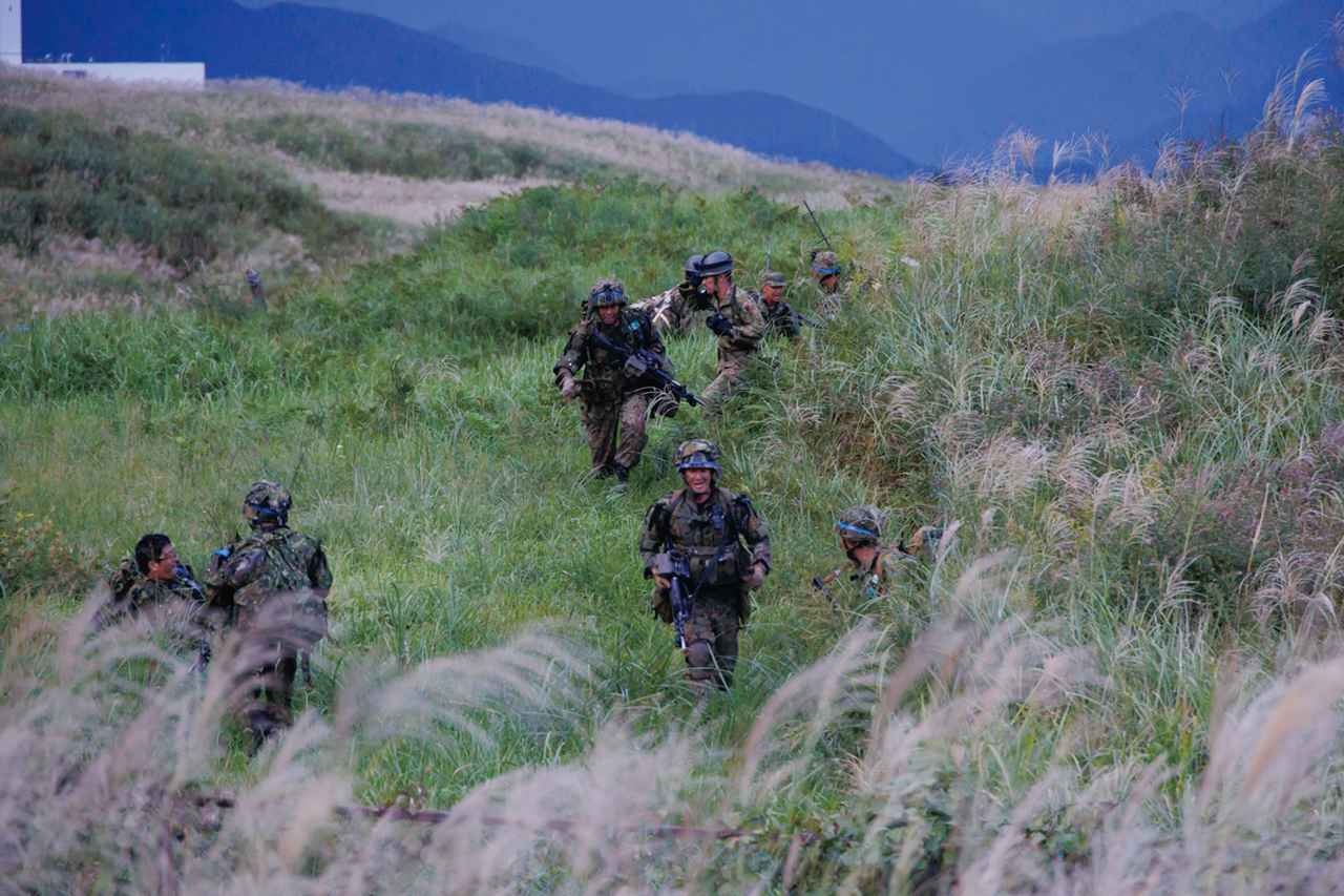 画像: ②茂みに身を隠し敵の陣地へと移動：攻撃の対象となる35普連の陣地に向けて移動する14普連の前線部隊。敵に見つからないように茂みへと足早に歩を進める　写真提供／防衛省