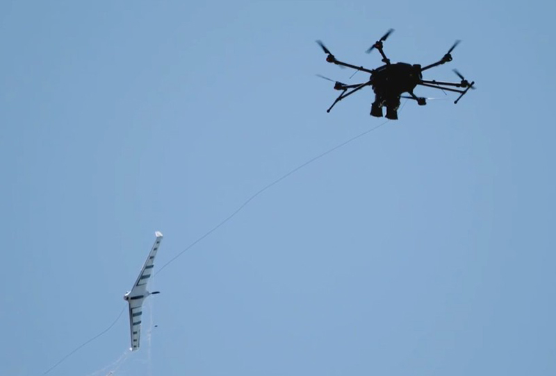 画像: 不審なドローン（写真左下）を発見し、ネットを発射して捕獲した東芝の自律型捕獲用ドローン。捕獲したドローンはこのまま安全な場所まで運搬して回収する
