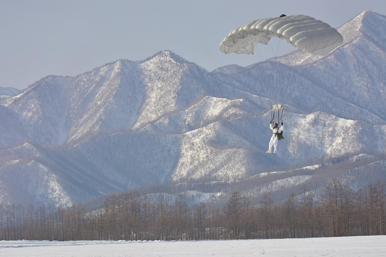 画像: 積雪地帯に降下する訓練。冬季積雪地用の白い装備を着用する。厚い積雪に埋もれてしまわないよう、慎重に着地する（写真提供／防衛省）