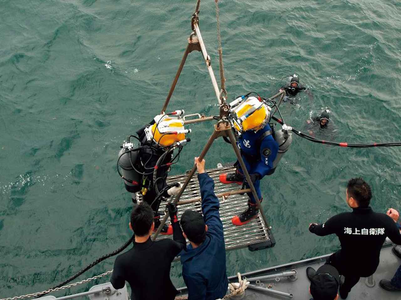 画像: 潜水訓練のため、専用の器材に乗り海に入る飽和潜水員。波や潮流にも対応できるよう訓練を重ねる