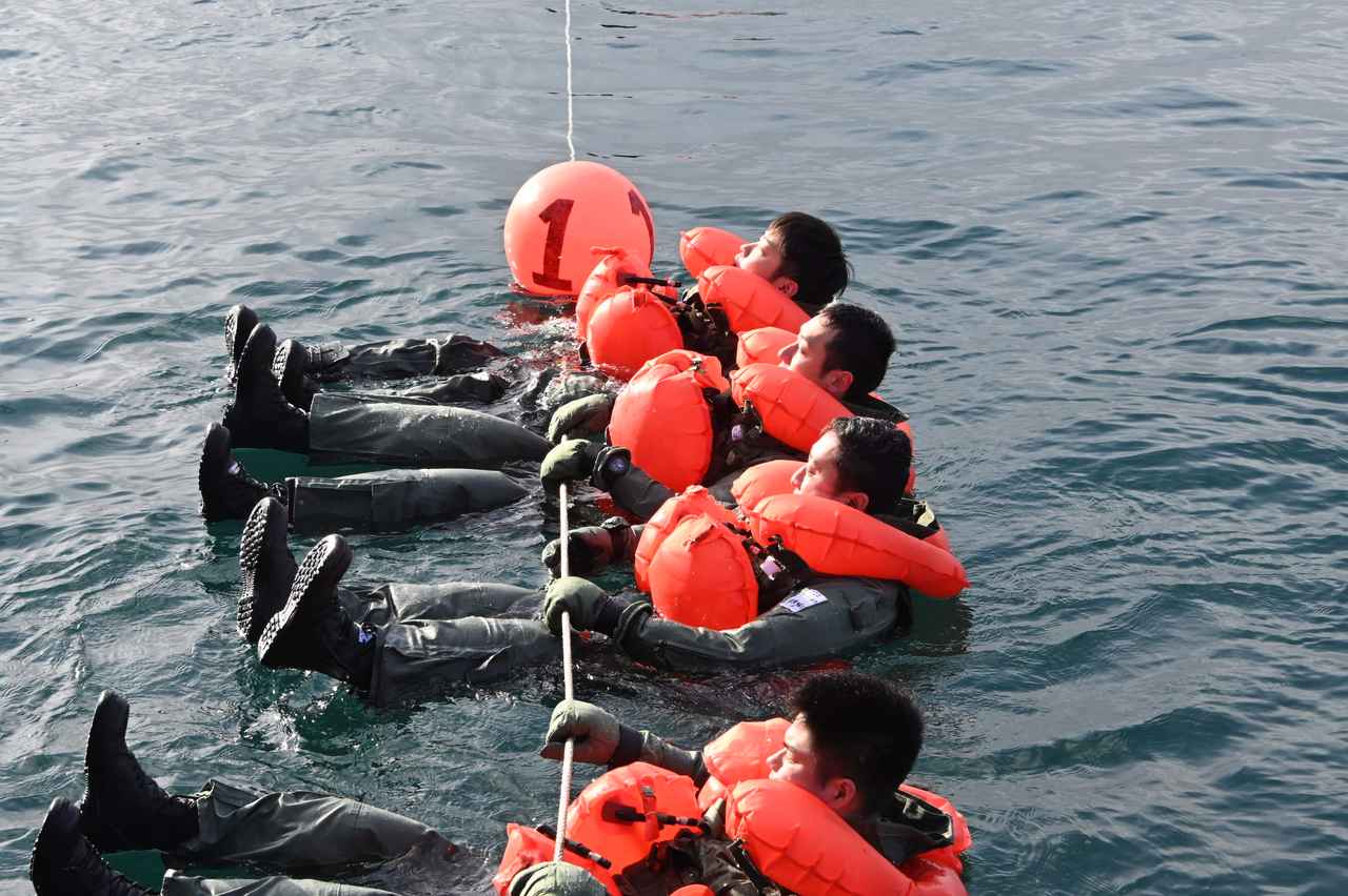 画像: 救命胴衣を着用し、訓練用ボートから投げられた1本のロープにつかまって海面に浮かぶ冬期救命生存講習