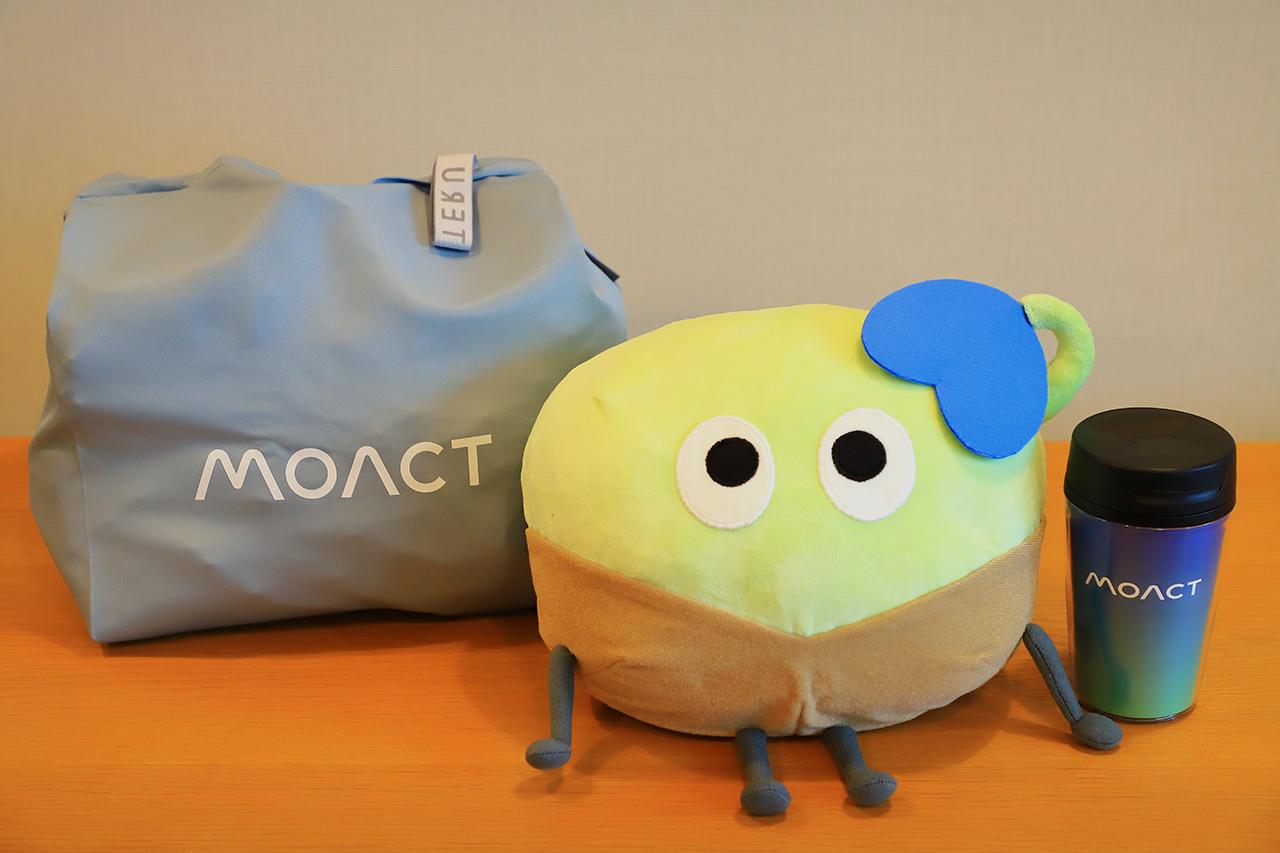 画像: モアクトのマスコットキャラクター「タネクト」のぬいぐるみの他、会社設立を記念して作成したというエコバッグとタンブラー（非売品）。
