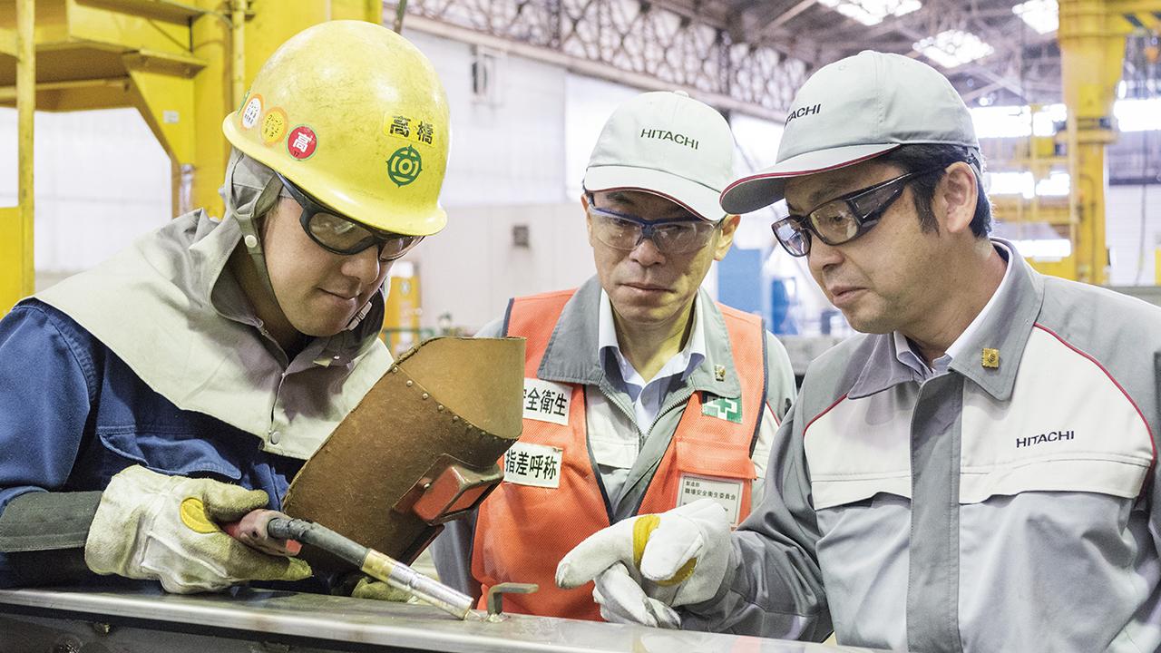 画像: 事業統括本部 受変電制御システム事業部 製造部 受変電システム製作課 組長 小室秀幸（中央）、高橋直樹（左）