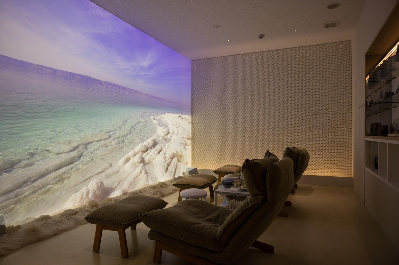 画像: スクリーンに映し出される死海のビジュアルと本物の死海の塩(床に注目!)を眺めながらハンドマッサージが受けられる「ヨルダンパビリオン」の「死海スパ」。20分¥2,500(実際の施術時間は10分程度)。予約は1Fカフェカウンターに相談を