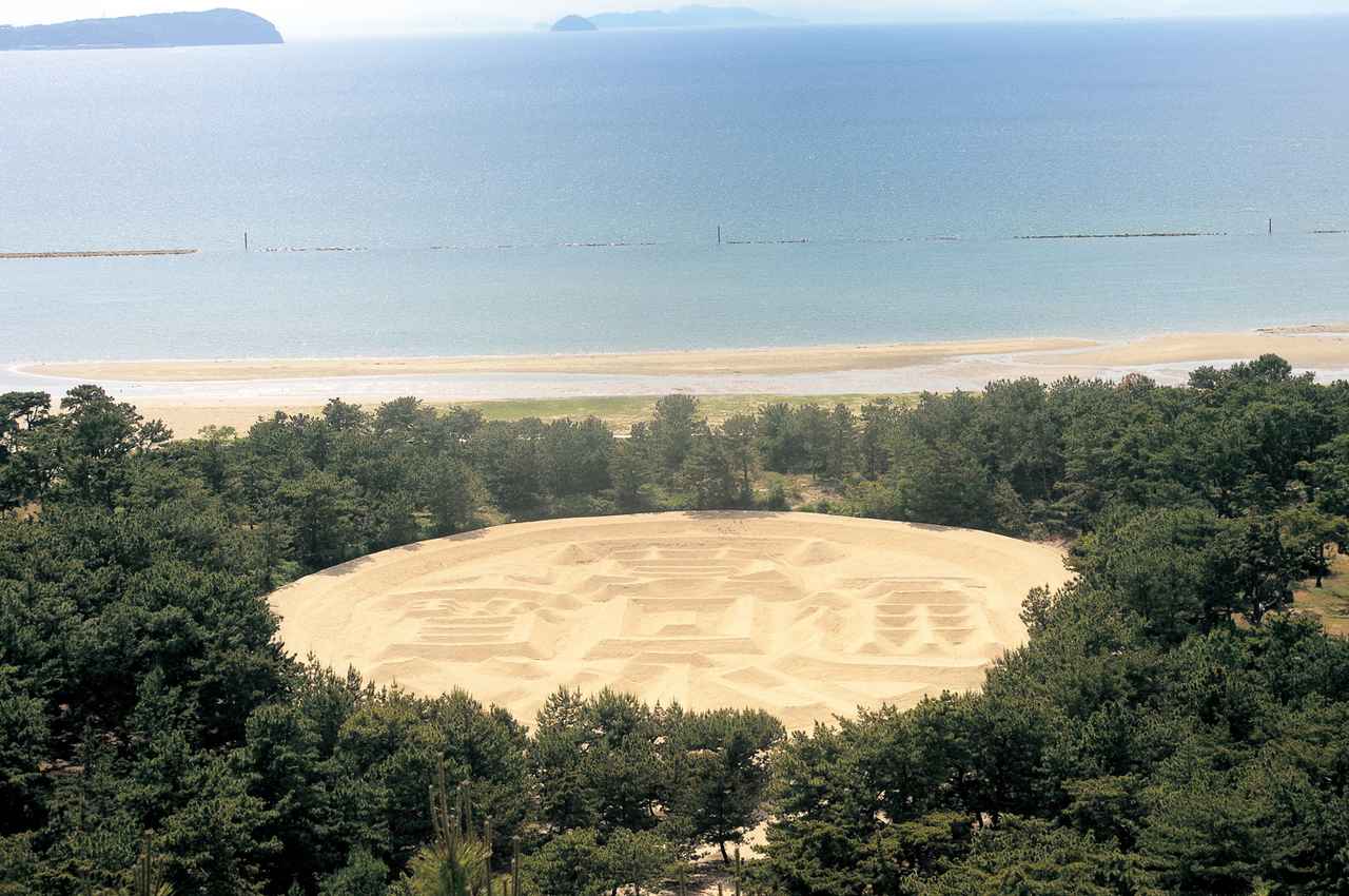 画像: ▲砂浜に描かれた縦122メートル、横９０メートルの巨大な砂絵、銭形砂絵「寛永通宝」。