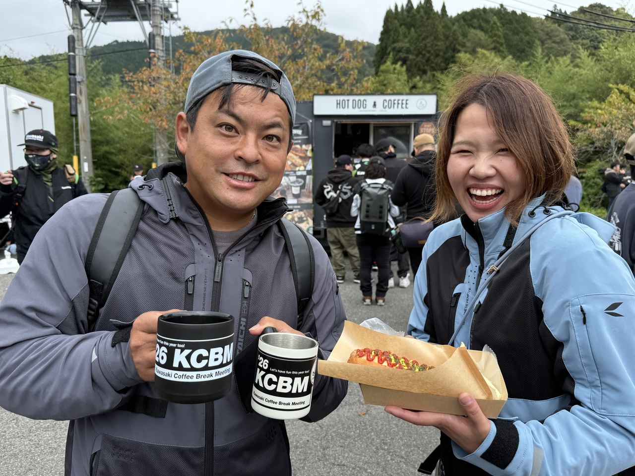 画像: ▲ ホカホカのホットドッグを笑顔で見せてくださったのは、イベント初参加のはまにし夫婦（広島）。旦那さんは2年前に購入したZEPHYR750、奥さんは10年乗ってるZRX1200 DAEGでご来場です‼